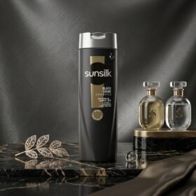 Sunsilk Black Shine Shampoo 360ml dark bottle displayed on a luxury metallic and marble podium with botanical accents by Chaudhary Superstore