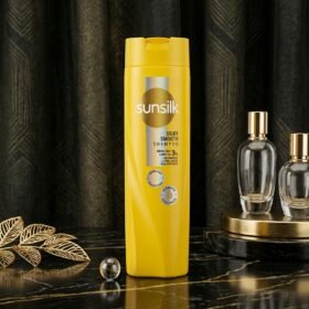 Sunsilk Silky Smooth Shampoo 360ml yellow bottle displayed on a luxury dark marble surface with botanical props by Chaudhary Superstore